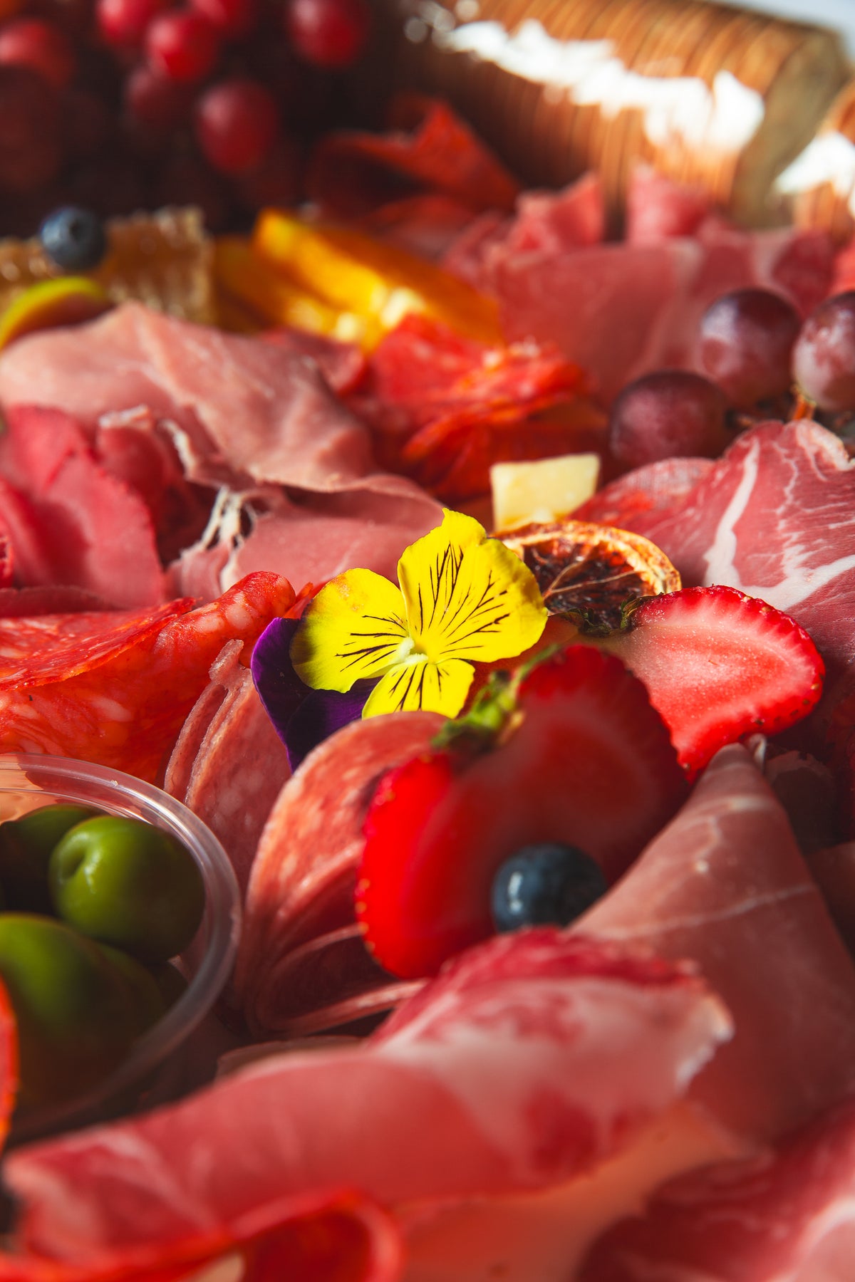 Assorted charcuterie, cheese and fruits with a yellow flower on a rustic charcuterie board