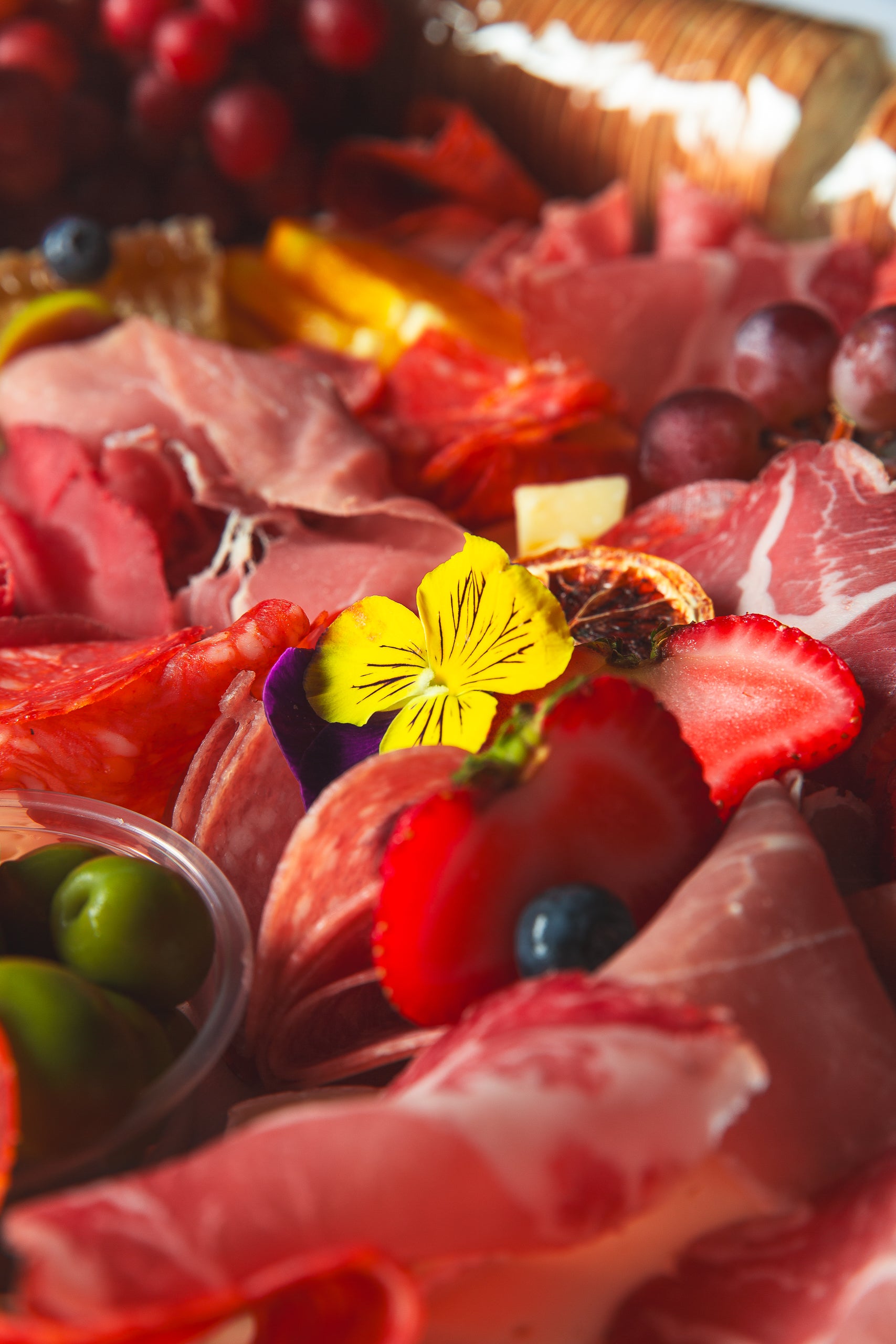 Assorted charcuterie, cheese and fruits with a yellow flower on a rustic charcuterie board