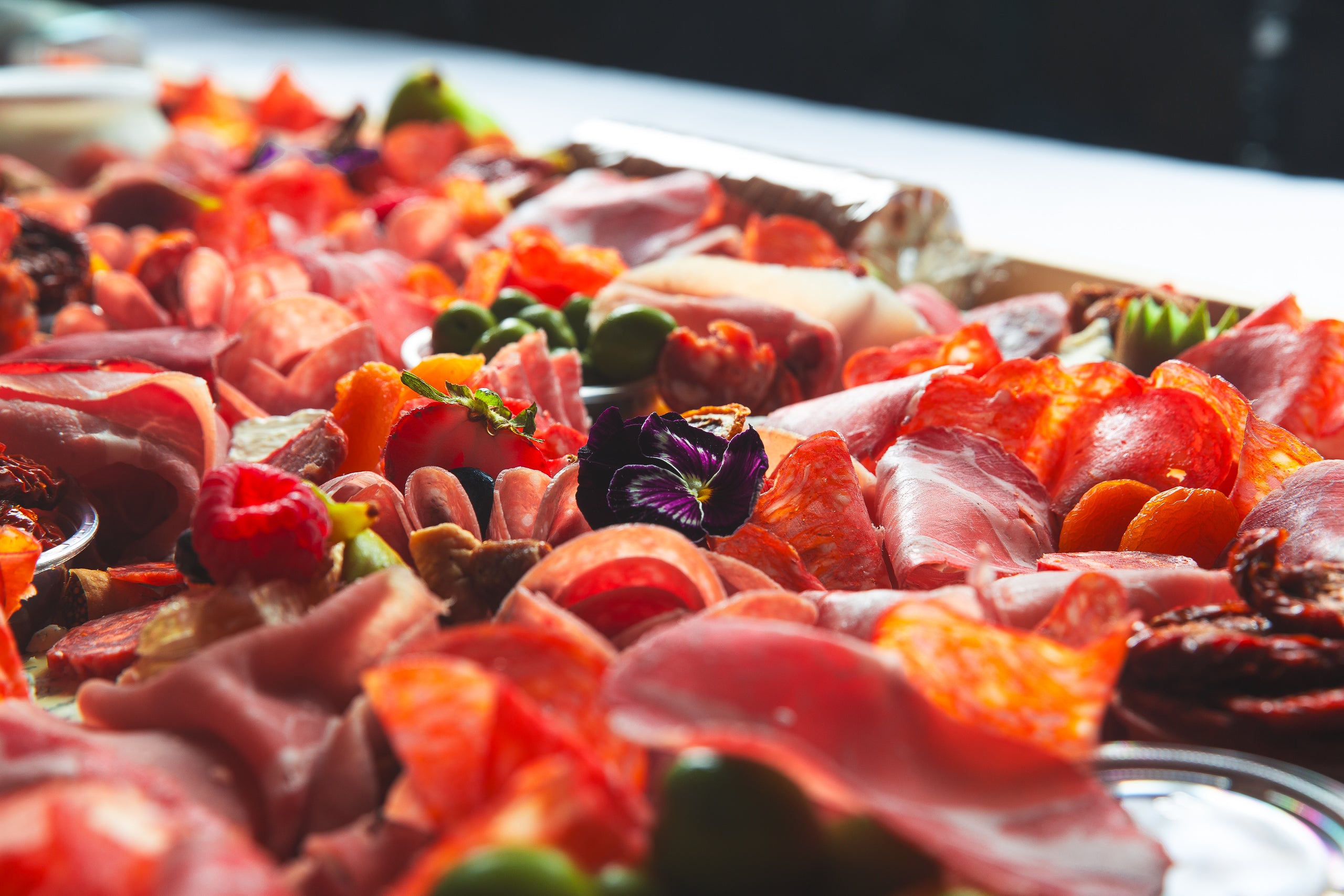 Platter of assorted cured charcuterie and fruits on charcuterie board on a white table for delivery in Toronto by The Graze Anatomy