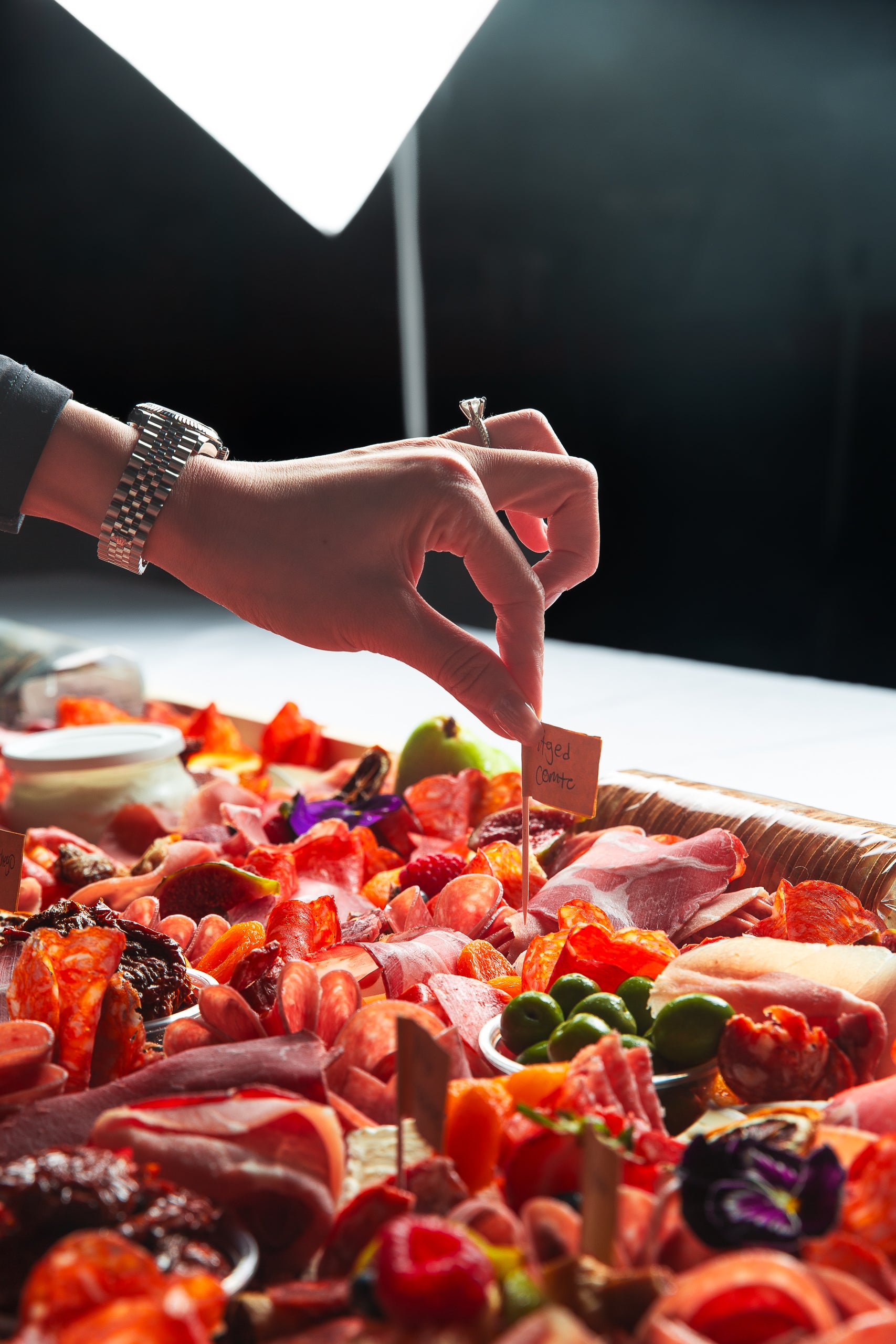 charcuterie board with a hand placing a descriptive flag on cheese and charcuterie